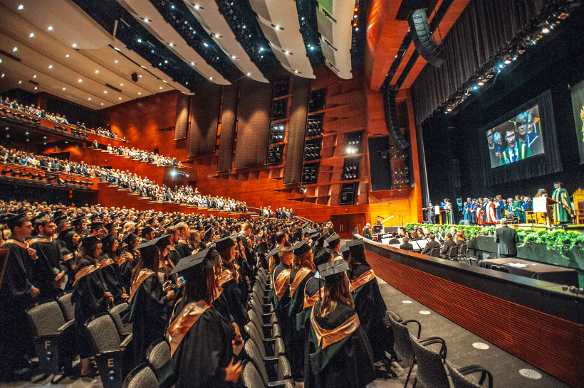 Image of convocation with students standing in a theatre watching a person deliver a speech